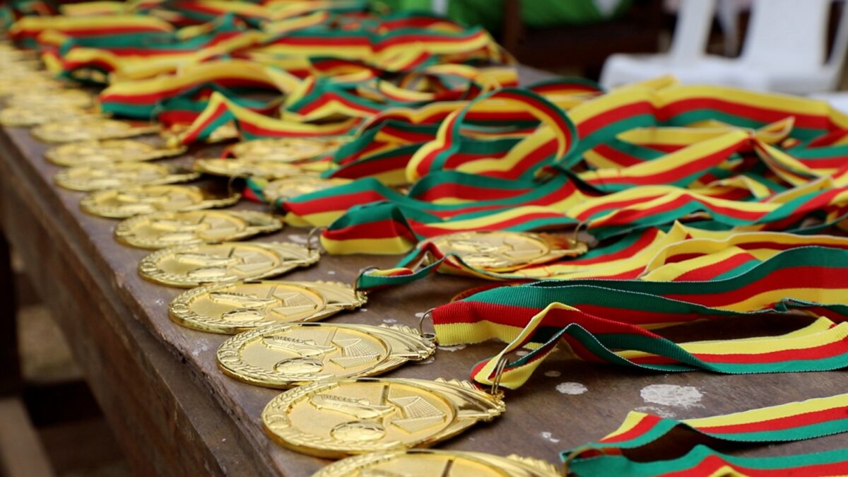Un plan moyen et légèrement surélevé montrant des médailles d'or disposées en rangées nettes sur une table en bois. Les rubans sont soigneusement pliés à côté de chaque médaille. La mise au point est nette sur les premières médailles, révélant des motifs de ballon de football et de joueur, et devient plus douce vers l'arrière-plan.
